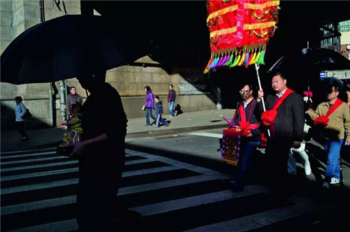 在纽约唐人街，你能看到各种各样的婚丧嫁娶习俗，图中一路接亲队伍穿过斑马线，显得怪异而离奇。
